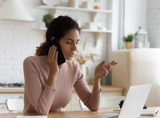 Confident young woman making phone call, sitting at table with laptop in kitchen, businesswoman freelancer working at home, consulting client or discussing project, having pleasant conversation